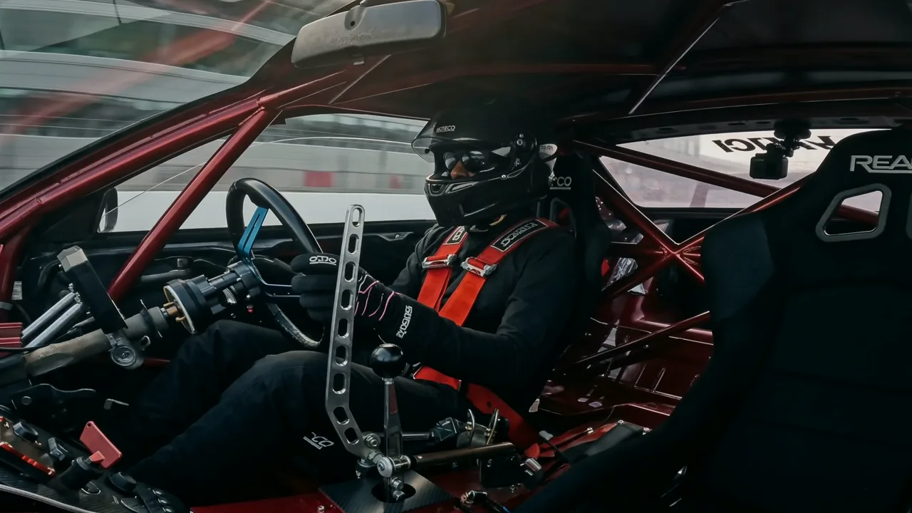 Daylight study of the race car cabin: red harness and roll cage against the circuit
