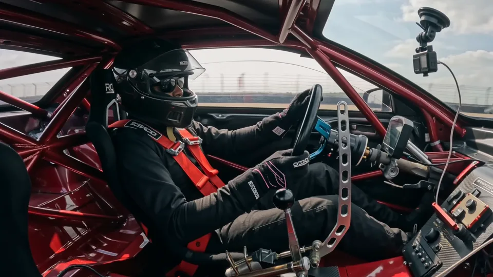 Race car cockpit hardware: quick-release wheel, harness, and roll cage in daylight