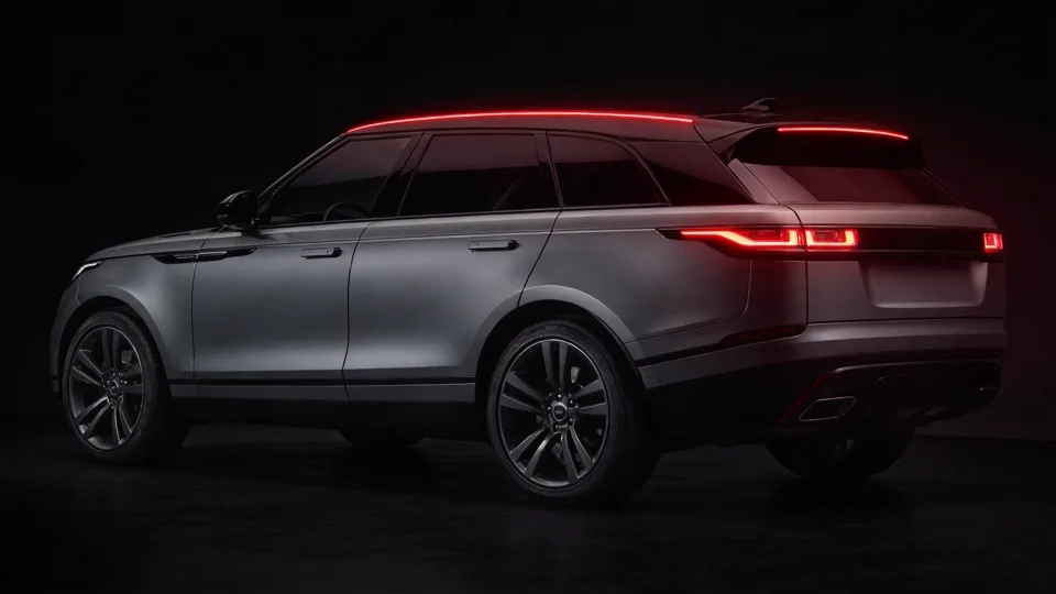 Luxury SUV in Velar proportions: level floating roof and slim full-width tail blade under deep red rim light